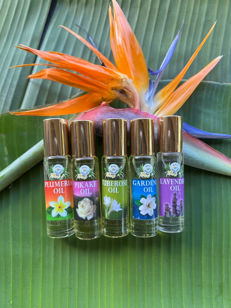 Maui Excellent Hawaiian Floral Roll-Ons: Plumeria, Pikake, Tuberose, Gardenia, and Lavender Oil leaning on a bird-of-paradise flower on a banana leaf.