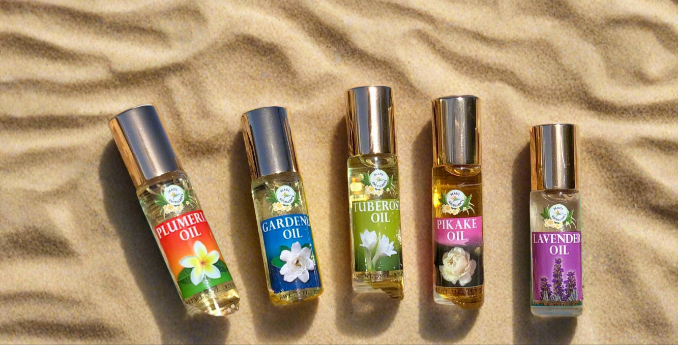All five Maui Excellent Hawaiian Floral Essential Oil Roll-On bottles are leaning on a small log on the sand.